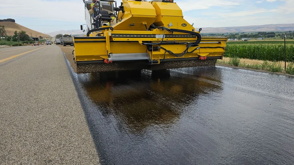 A paving machine laying a fresh mat of black asphalt across an open lot