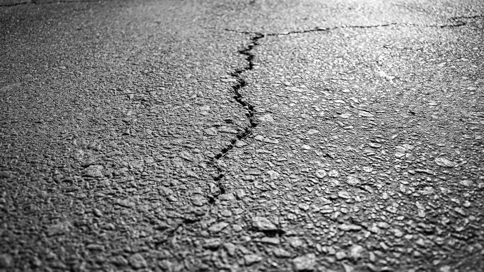A crack spreading across an aging asphalt surface